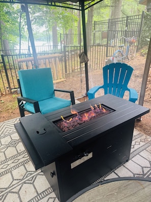 A patio area with a black grill, blue chairs, and a view of a wooded area.