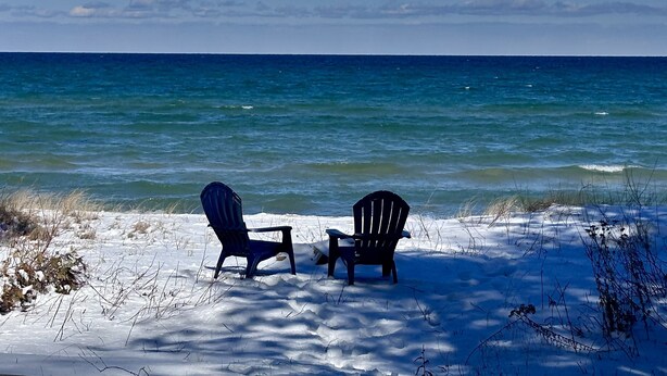 Two Adirondack chairs facing a beach with a view of the ocean.
