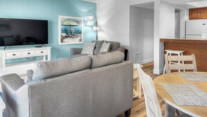A modern living room with a grey sofa, a flat-screen TV, and a painting on the wall. - Beautiful Two Bedroom Condo at Midnight Cove II (Siesta Key)