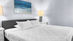 A neatly made bed with a white quilt, a grey headboard, and a painting of Georgia O'Keeffe on the wall. - Beautiful Two Bedroom Condo at Midnight Cove II (Siesta Key)