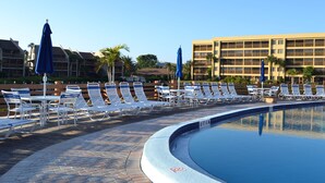 A poolside area with lounge chairs and umbrellas, a pool, and a hotel building in the background. - Beautiful Two Bedroom Condo at Midnight Cove II (Siesta Key)
