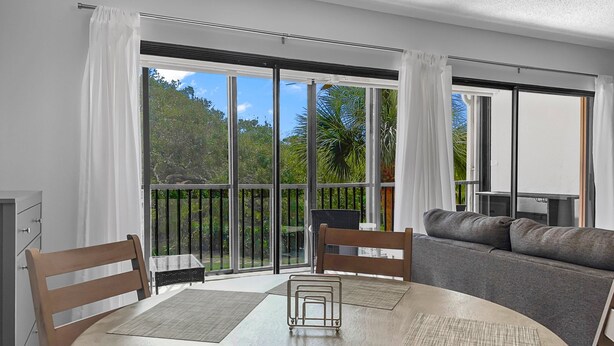A modern living room with a round dining table, two wooden chairs, a grey sofa, and a balcony with large sliding glass doors. - Beautiful Two Bedroom Condo at Midnight Cove II (Siesta Key)