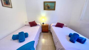 Una habitación con dos camas, cada una con una toalla azul, una mesita de noche de madera con lámpara y un cuadro en la pared.