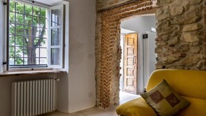 Een kamer met een stenen muur, een gele bank, een raam met uitzicht op bomen, en een radiator.