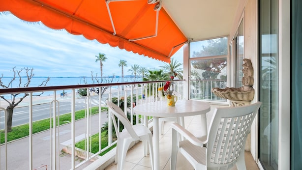 En balkon med et hvidt bord og stole, en orange markise og udsigt til gaden og palmer.