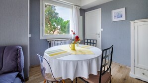 Et spiseområde med et rundt bord, stole, en vase med blomster, en radiator og et vindue med gardiner.