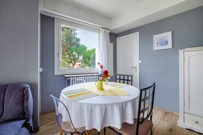 A dining area with a round table, chairs, a vase with flowers, a radiator, and a window with curtains.