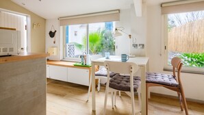 A modern kitchen with a dining area, white cabinetry, and a large window with a view of greenery. - Petite House-Studio with Terrace and Garden (cagnes sur mer)