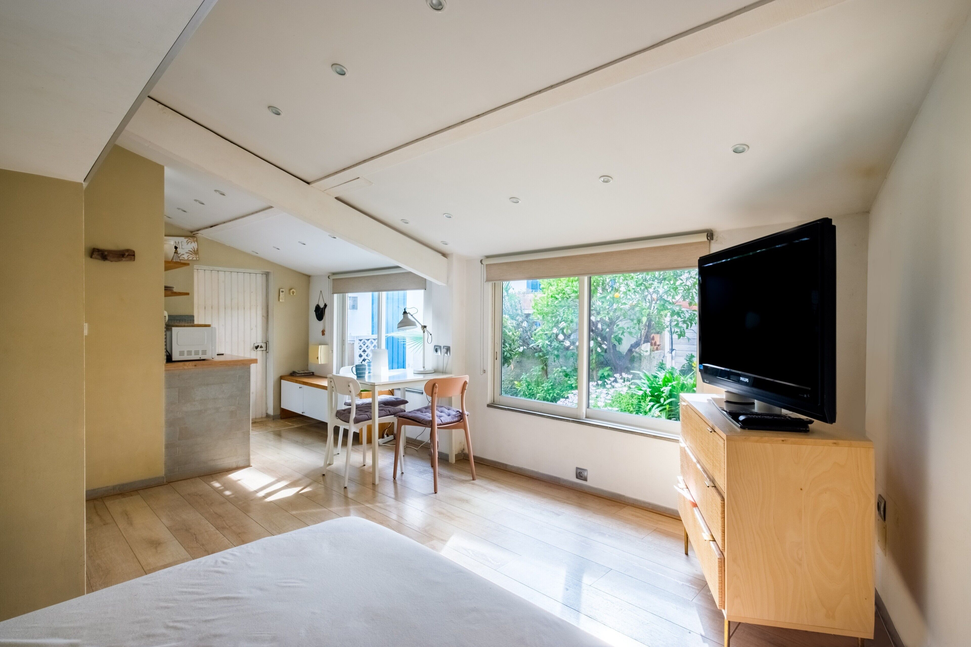 Ein modernes Zimmer mit einem Bett, einem Fernseher, einem Schreibtisch mit Stuhl und einem Fenster mit Blick auf Grünflächen.