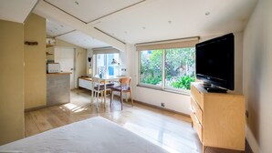 A modern room with a bed, a TV, a desk with a chair, and a window with a view of greenery. - Petite House-Studio with Terrace and Garden (cagnes sur mer)
