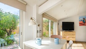 A modern room with a white table, two chairs, a TV, and a large window overlooking greenery. - Petite House-Studio with Terrace and Garden (cagnes sur mer)