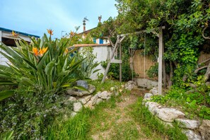 Ein Garten mit einer Holz-Pergola, einer Steinmauer und unterschiedlichen Pflanzen.