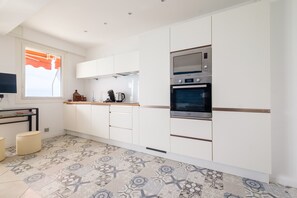 Una cocina moderna con armarios blancos, horno empotrado y piso estampado.