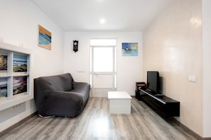 A living room with a sofa, a TV, a white coffee table, and artwork on the walls. - Apartment 'Piso Pablo' with Private Terrace and Wi-Fi (Barbate)