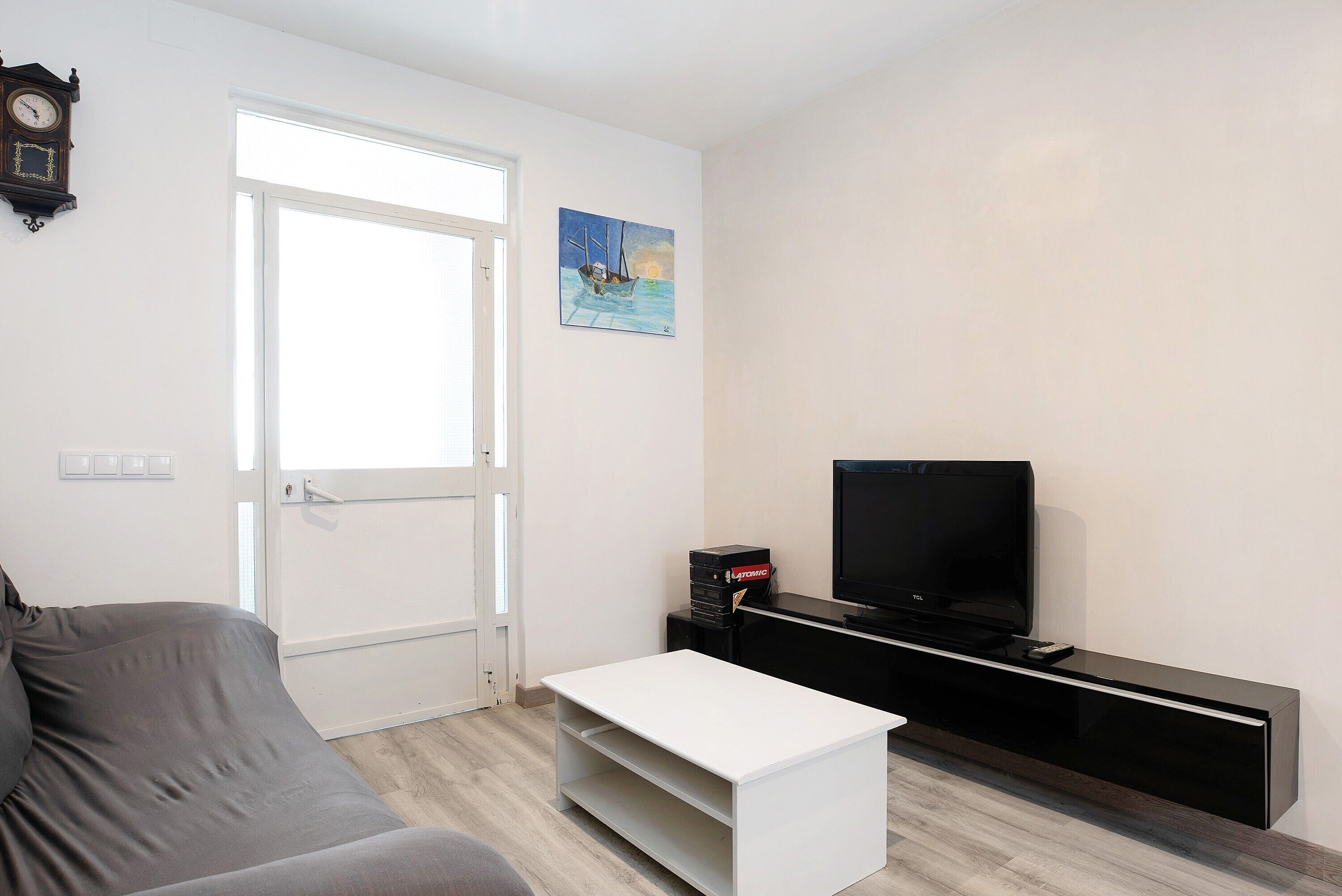 A living room with a sofa, a flat-screen TV, a coffee table, a painting, and a clock on the wall.