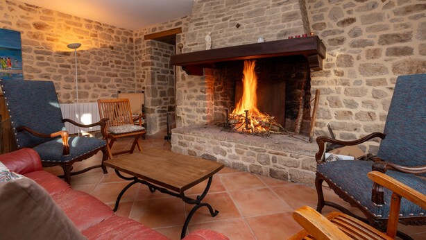 Una habitación con paredes de piedra, una chimenea, dos sillones tapizados, una mesa de madera y un sofá rojo.