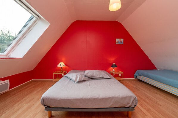 A room with a sloped ceiling, a bed, a bedside table with a lamp, a small table with a lamp, and a window.