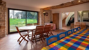 Un comedor con una mesa grande y sillas, un muro de piedra y vistas a un jardín.