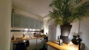 A compact kitchen with a microwave, stove, sink, and a potted plant. - Bright Apartment in Batignolles – Parisian Charm, Self Check-In (Paris)