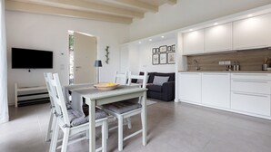Eine moderne Küche mit weißen Schränken, ein Essbereich mit Tisch und Stühlen sowie ein an der Wand befestigter Flachbildfernseher.
