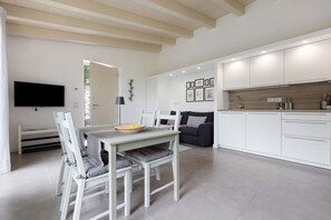 Une cuisine moderne avec des meubles blancs, un coin repas comprenant une table et des chaises, et un téléviseur à écran plat fixé au mur.