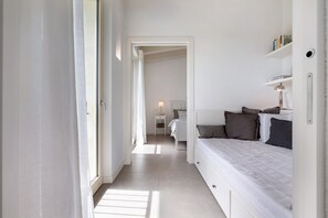 A narrow hallway leading to a bedroom with a bed, bedside table, and a lamp.