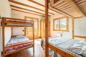 Une chambre avec un lit superposé, des poutres en bois, une fenêtre et une vue sur l’extérieur.