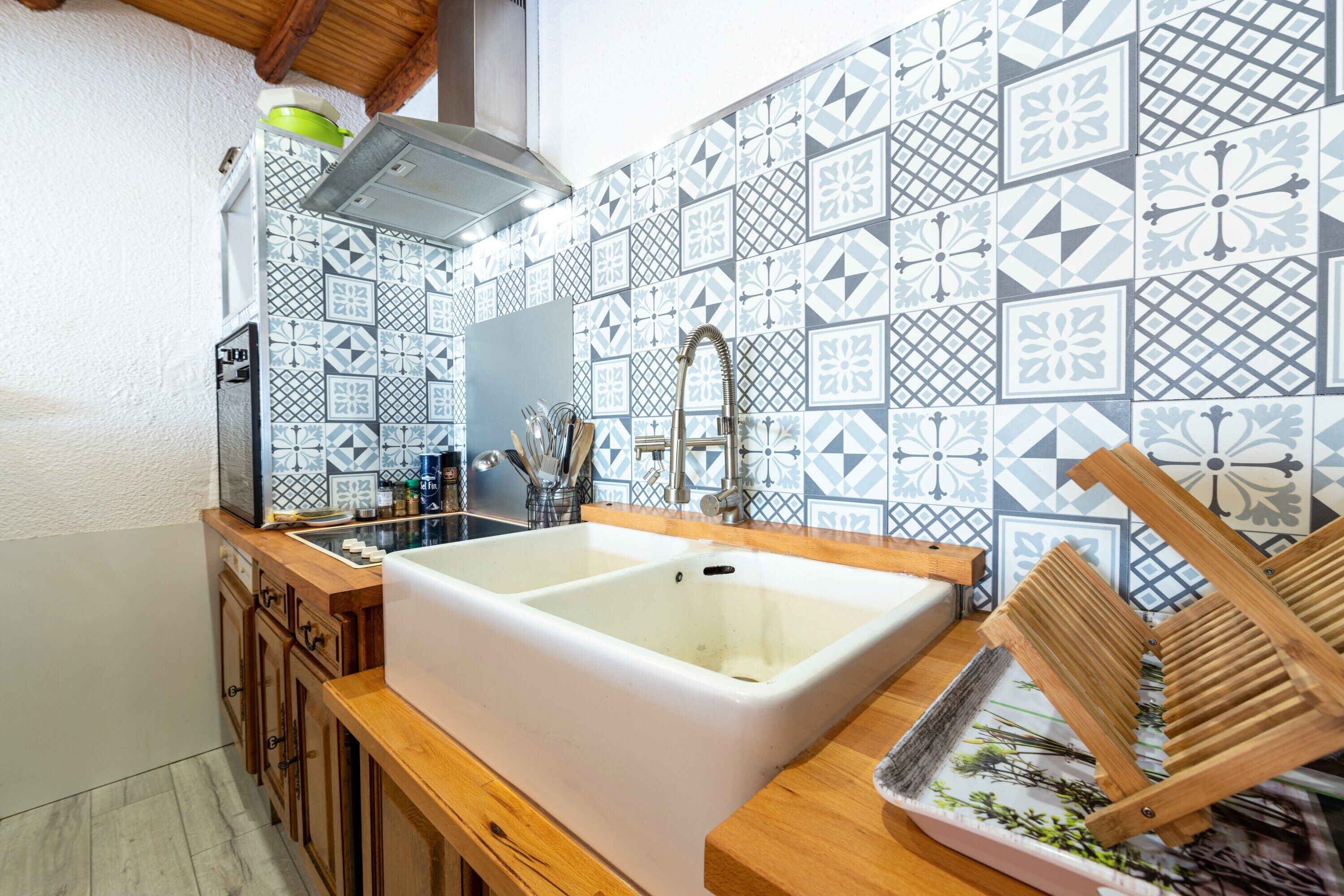 Une cuisine dotée d’un grand évier blanc, de meubles en bois et de carreaux décoratifs sur le mur derrière l’évier.