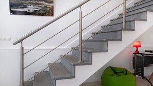 Een trap met metalen leuningen, een groene relaxstoel, een rode lamp en een aan de muur hangend schilderij.