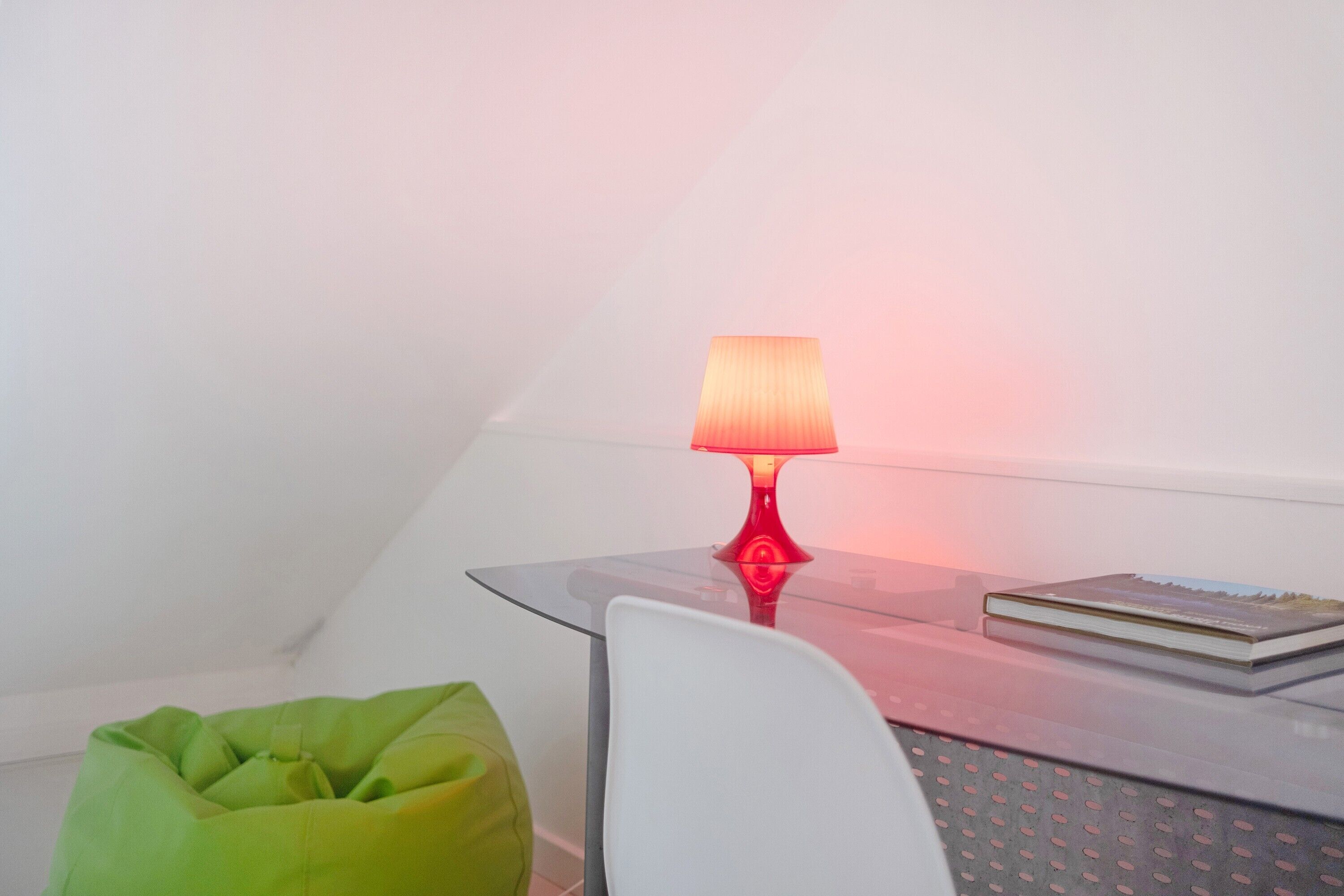 A glass table with a red lamp, a green bean bag chair, and a book.