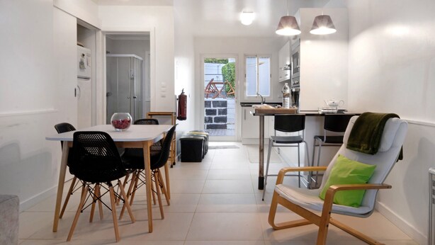 Een moderne keuken met een eethoek, een stoel met een groene kussens en een kleine tafel met een schaal fruit.