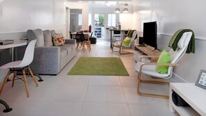 Een moderne woonkamer met een bank, stoelen, een televisie en een eethoek.