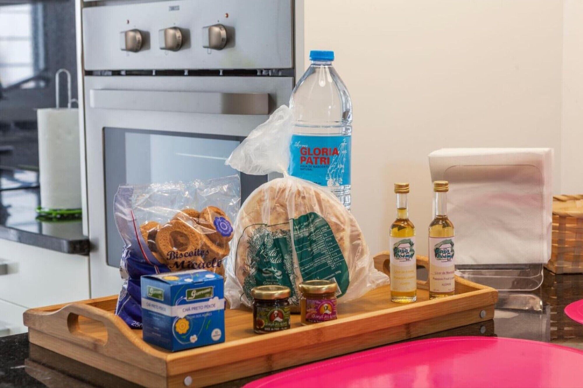 A kitchen counter with a loaf of bread, a water bottle, a bag of pretzels, a box of tea, and two bottles of olive oil.