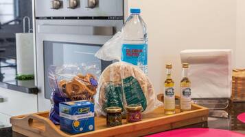 A kitchen counter with a loaf of bread, a water bottle, a bag of pretzels, a box of tea, and two bottles of olive oil.