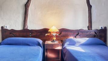 Une chambre avec deux lits, une tête de lit en bois, une table de chevet avec une lampe et une prise électrique au mur.