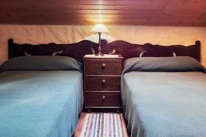 A bedroom with two twin beds, a wooden headboard, a nightstand with a lamp, and a striped rug.