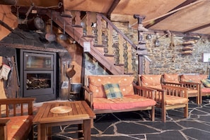 A rustic interior with a stone fireplace, wooden staircase, and seating area.