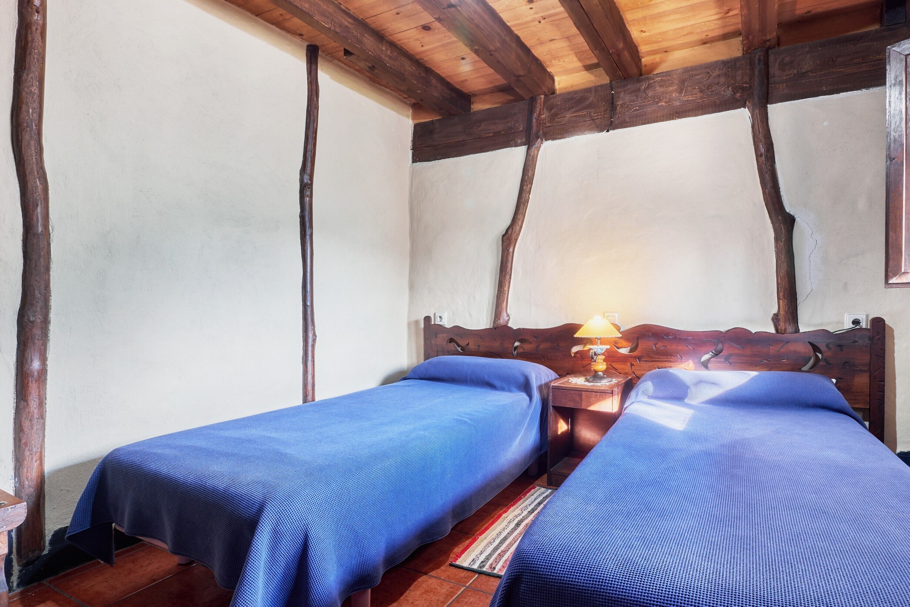 Una habitación con dos camas, vigas de madera en el techo y una mesita de noche con lámpara.