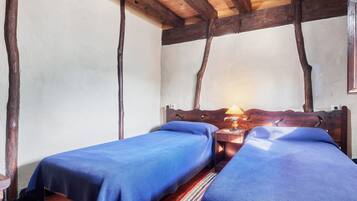 Una habitación con dos camas, vigas de madera en el techo y una mesita de noche con lámpara.