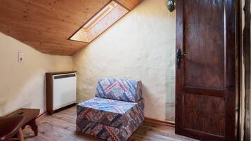 Una habitación con techo inclinado, un banco de madera, un sofá estampado, una puerta y un radiador.