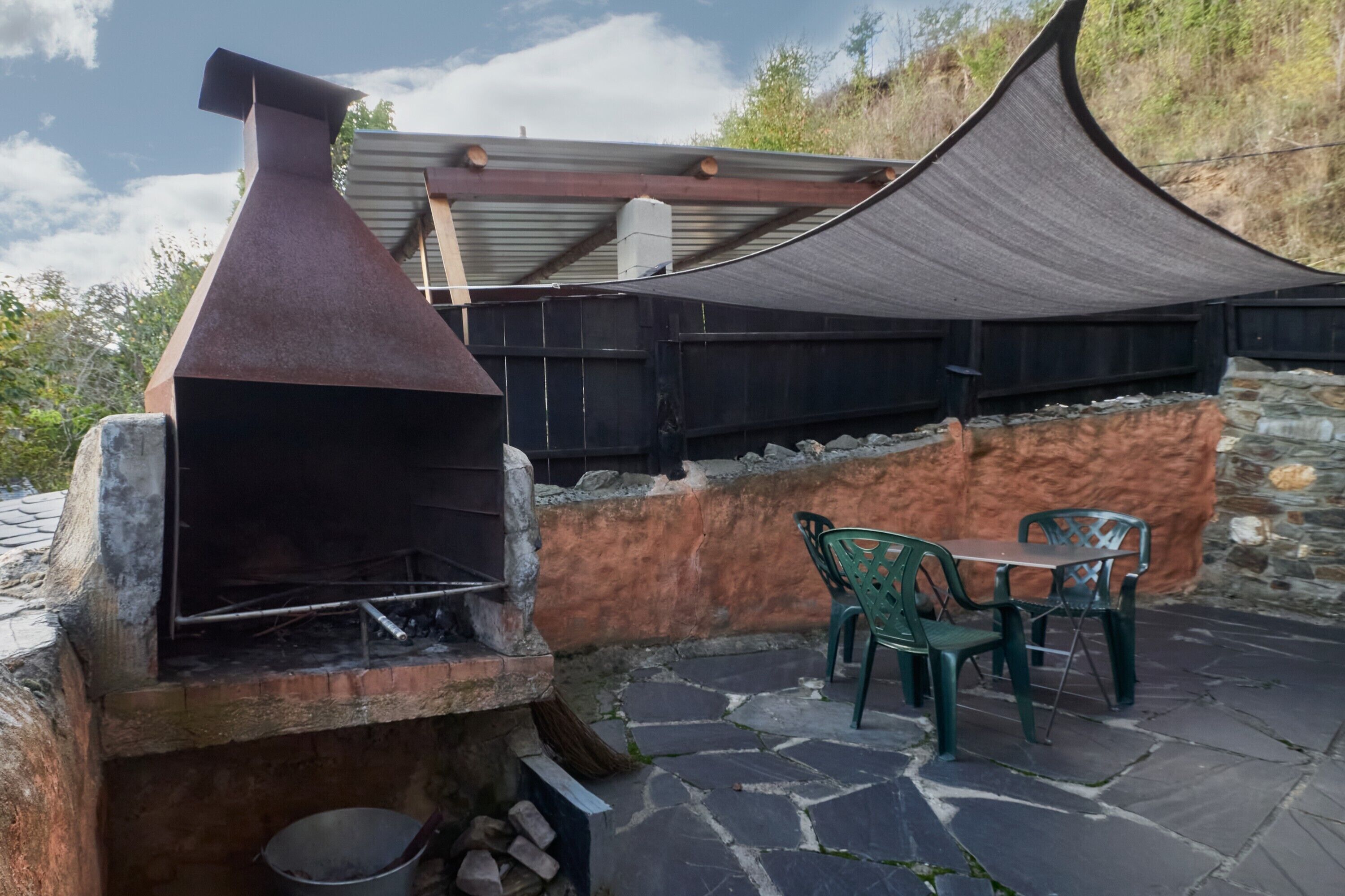 Un patio de piedra con una parrilla, dos sillas verdes y una mesa.