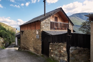 A stone building with a wooden balcony, a chimney, and a sign indicating a call to action.