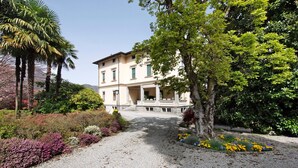 A building with a gravel driveway, surrounded by various plants and trees. - Apartment 'Historia Suite Bellagio' with Lake View, Shared Garden and Wi-Fi (Bellagio)