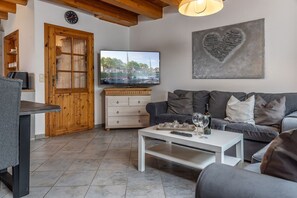 Uma sala de estar com televisão, mesa de centro branca, sofá cinza e um armário de madeira.