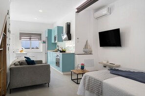 Ein modernes Zimmer mit Bett, Sofa, kleinem Tisch, Fernseher und einer Küchenzeile mit Schränken und Geräten.