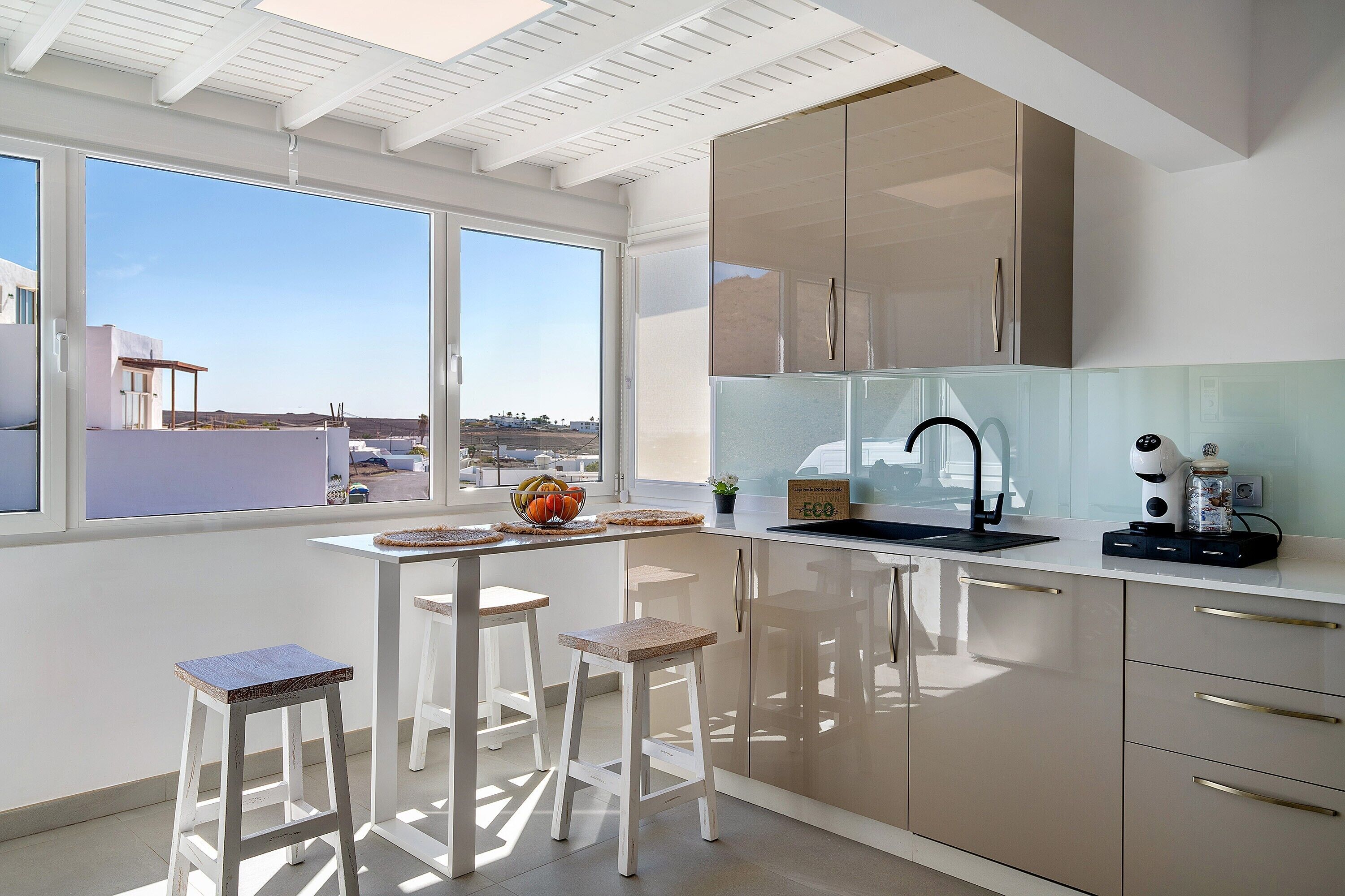 Una cocina moderna con un ventanal grande, muebles blancos y dos taburetes.