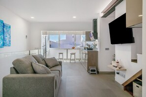 Un soggiorno moderno con un divano, una TV a parete e un angolo cottura con sgabelli.