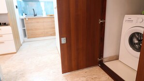 Un espace buanderie avec un lave-linge, une porte en bois et, au fond, une cuisine.