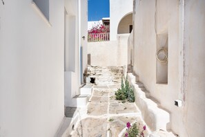 A narrow stone pathway leading to a white building with a balcony and a flower box. - Central Holiday Apartment 'Olga's House kythnos D' (??????)