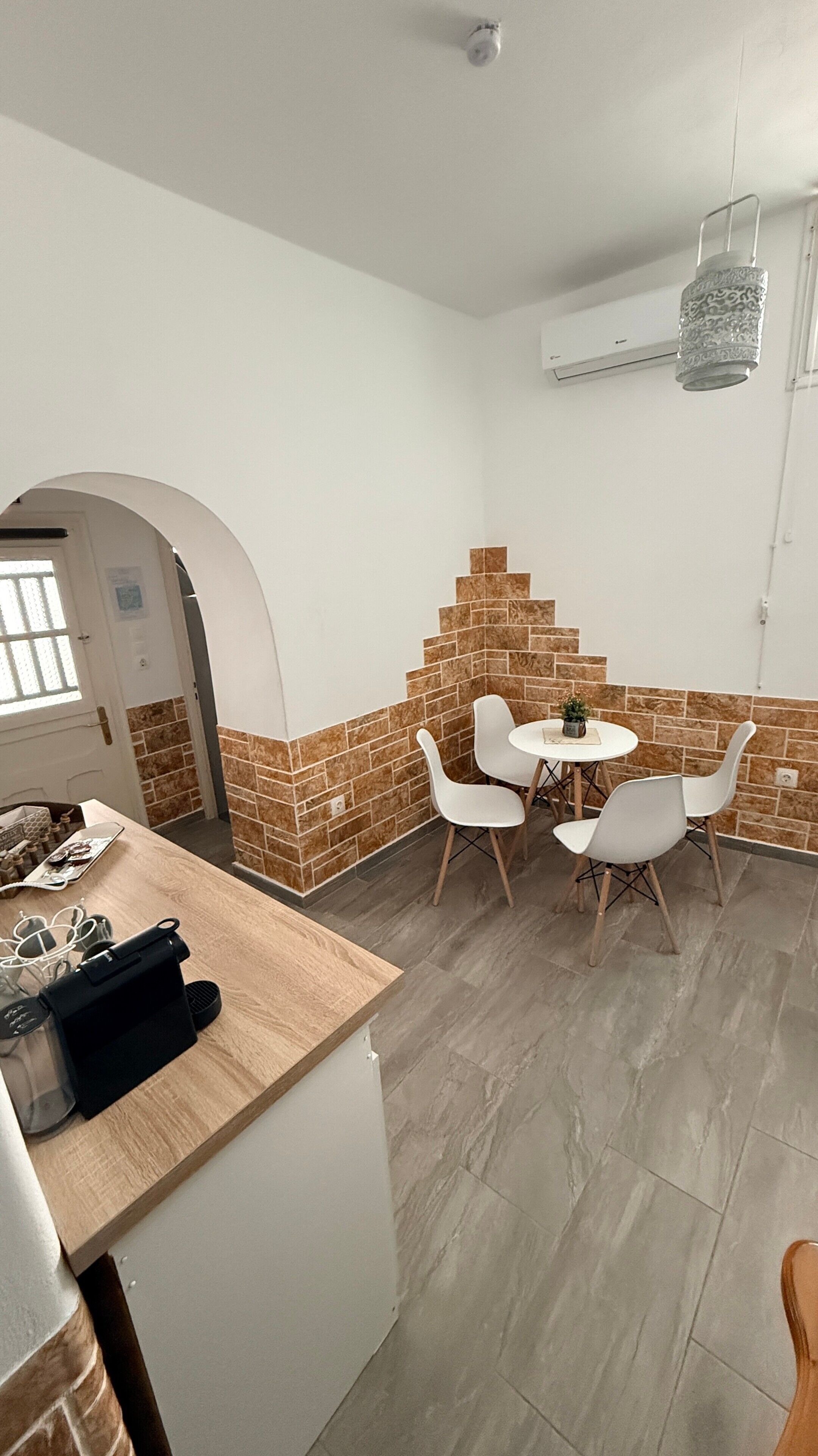 Eine Küche mit Holzarbeitsplatte, Spüle und Fenster. Es gibt eine Essecke mit Tisch und Stühlen sowie eine Wand mit Ziegelmuster.